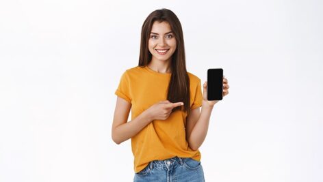 تصویر دختر جوان با لبخند و اشاره کردن به موبایل