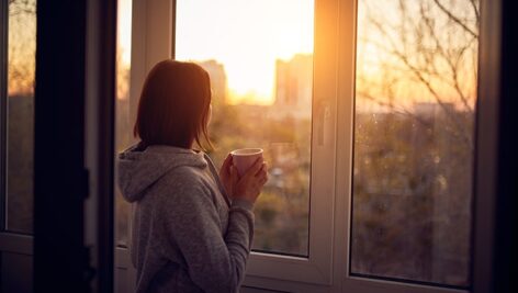 تصویر پس زمینه زن جوان در کنار پنجره و غروب آفتاب