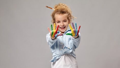 تصویر دختر بچه با دستان رنگی در حال نقاشی کشیدن