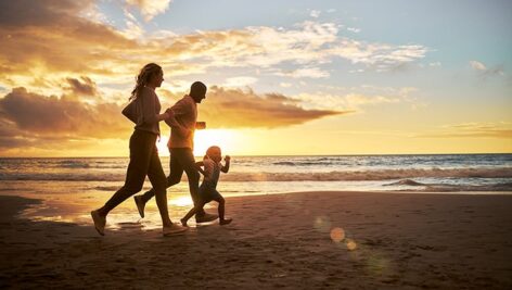 تصویر خانواده شاد در حال دویدن در ساحل دریا و غروب