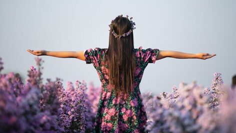 تصویر زن جوان با دستان باز در میان گل ها